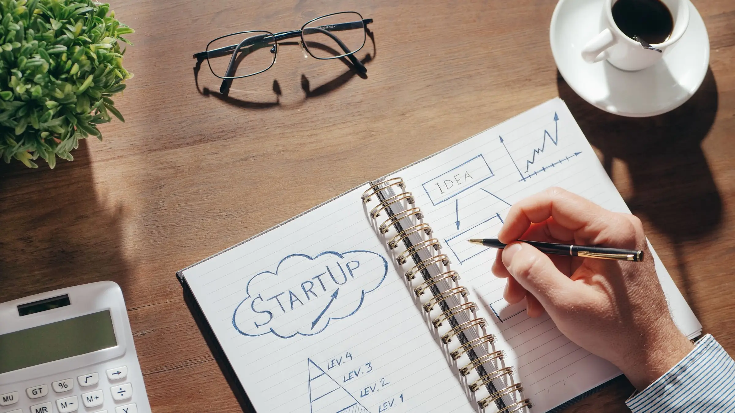 Mesa de trabajo con un cuaderno de plan de negocio, gráficos impresos y un portátil